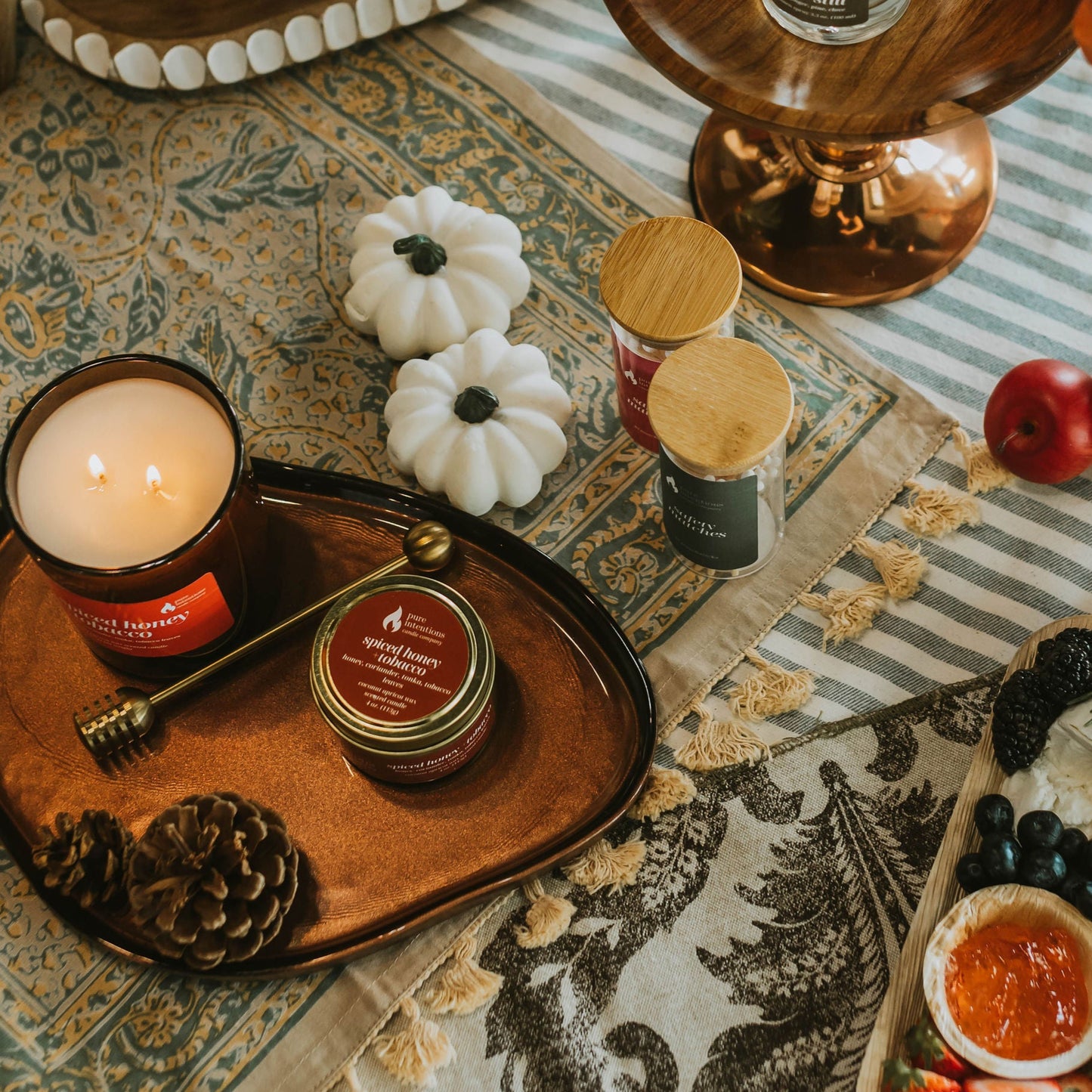 Table setting with candles, small containers, and a charcuterie board on a patterned tablecloth.