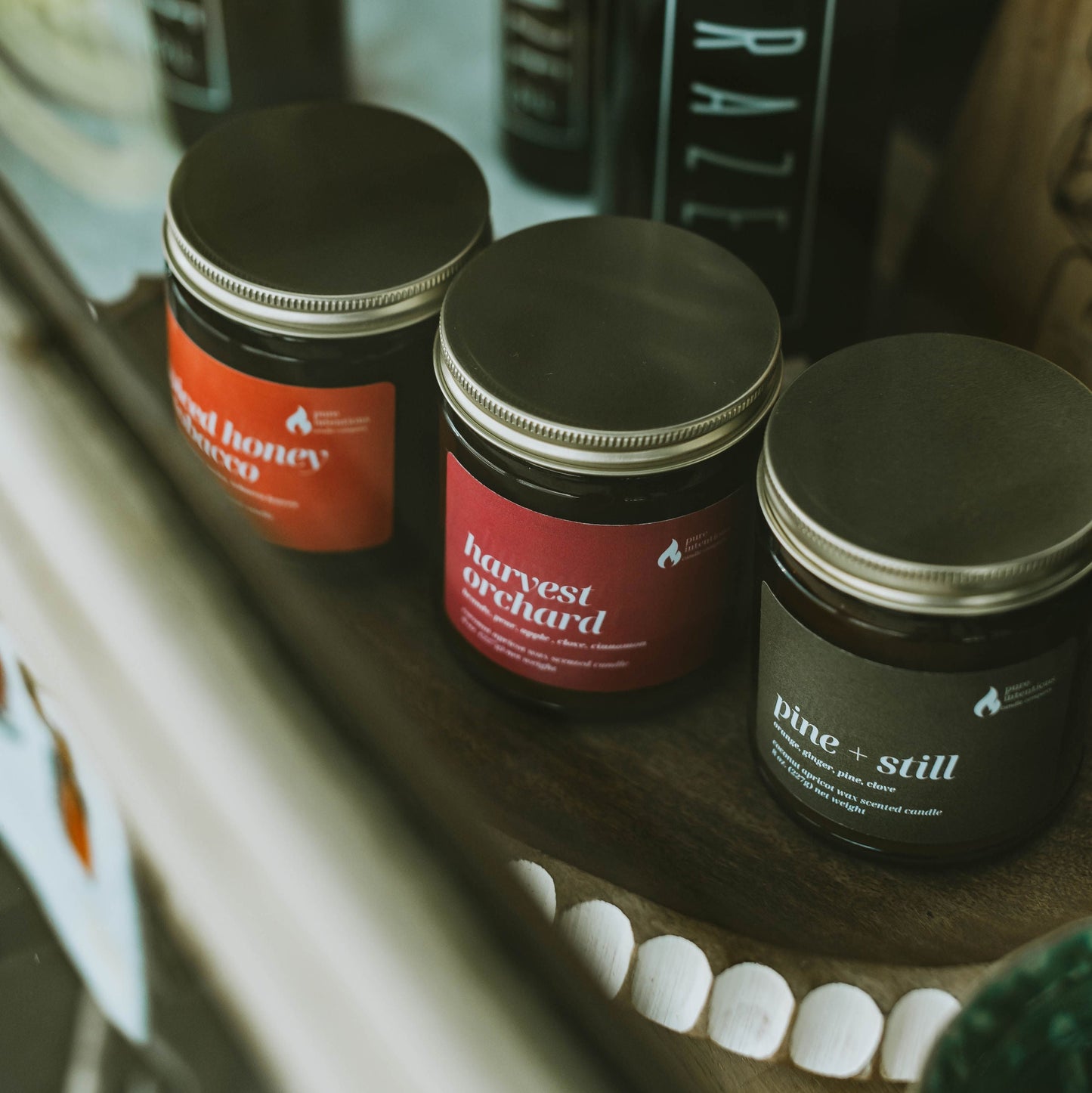 Jars of different sizes with labels on a shelf, with a bottle in the background.