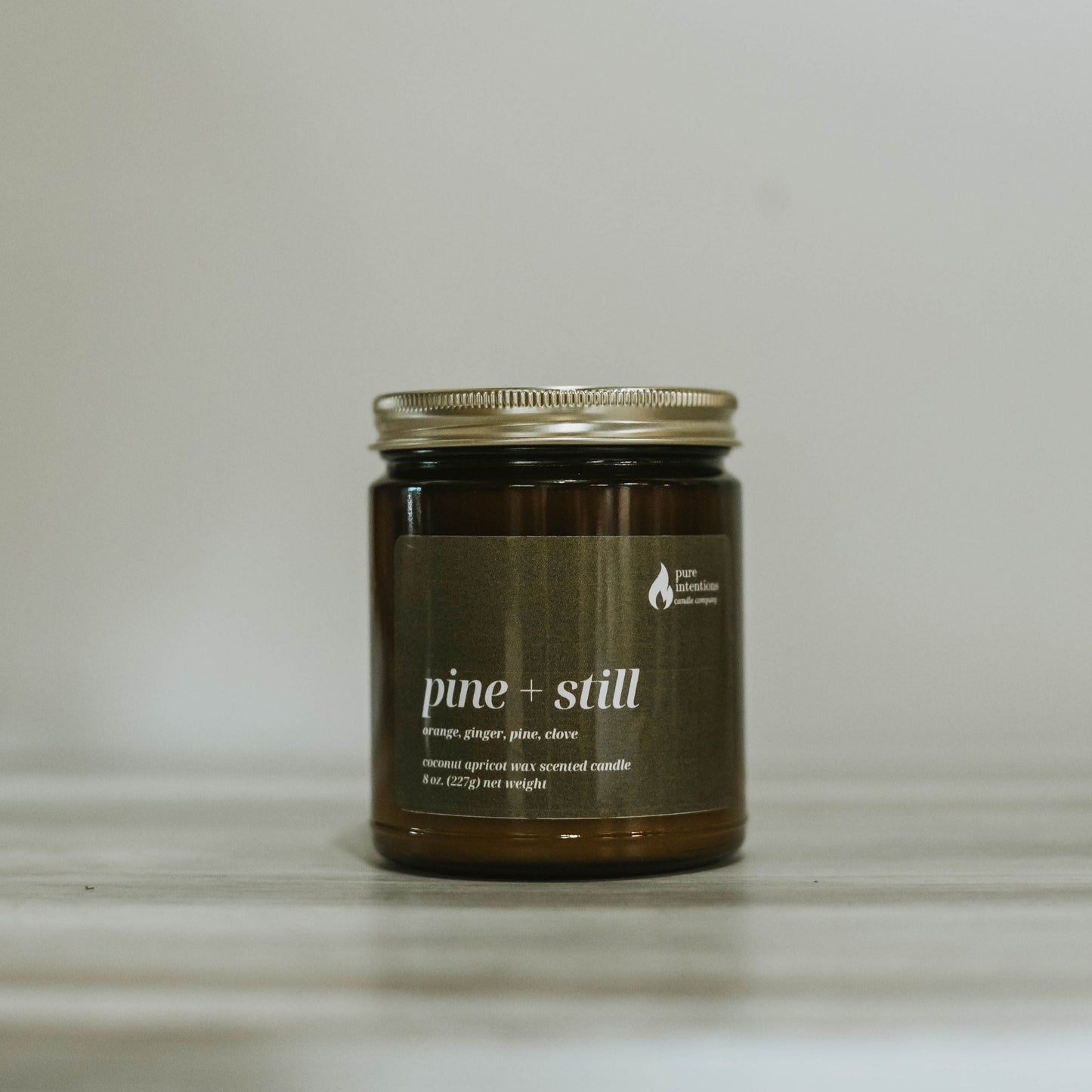 Candle jar labeled 'pine + still' on a neutral background