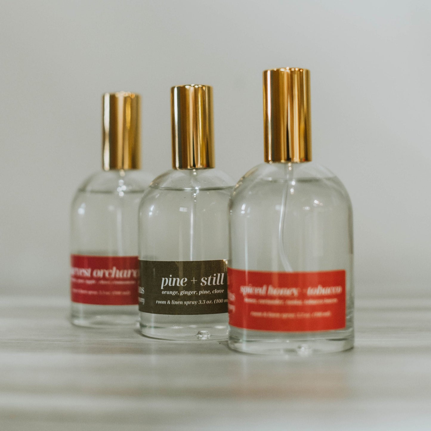 Three bottles of room and linen spray on a light surface with a neutral background