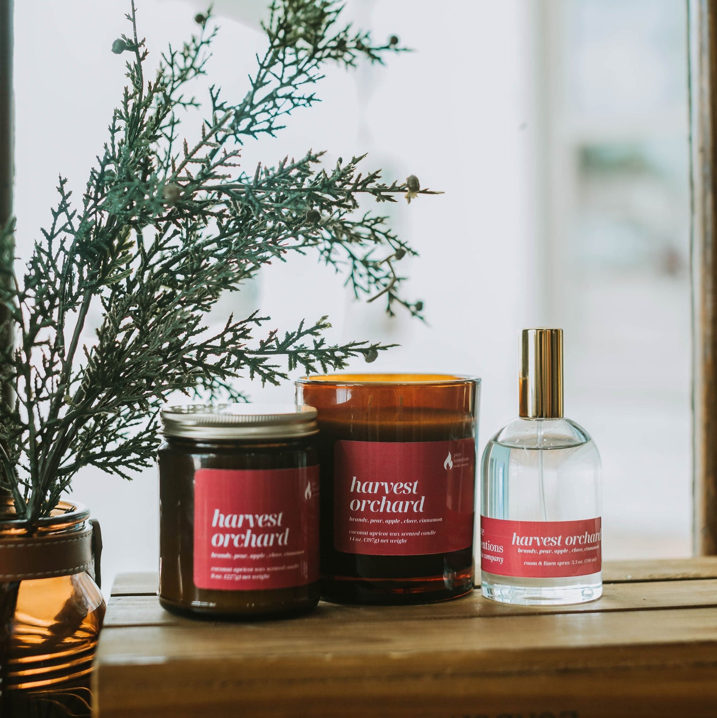 Harvest Orchard candles and a bottle on a wooden surface with a blurred window background