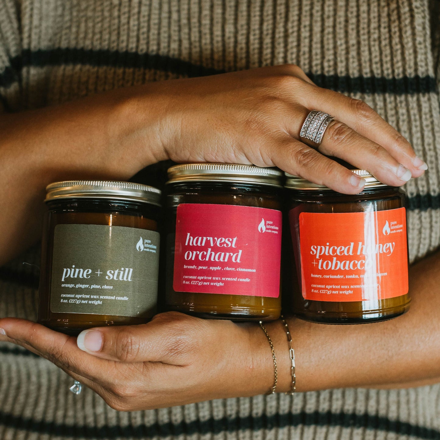 Person holding three jars of different scents against a striped sweater background
