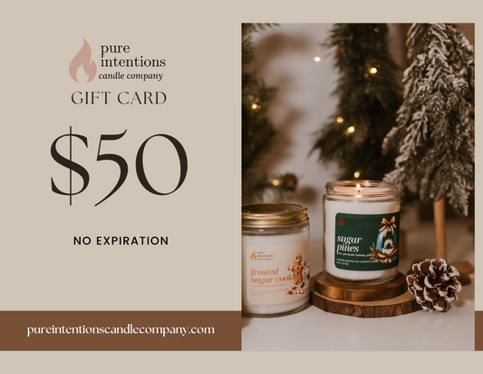 Pure Intentions Candle Company digital gift card, valued at $50. The card displays the brand’s logo and features two candles—"Sugar Pines" and "Frosted Sugar Cookie"—in a warm, wintery setup with festive decor, including a pine cone and snowy pine trees. The phrase "No Expiration" and the company’s website URL are included.