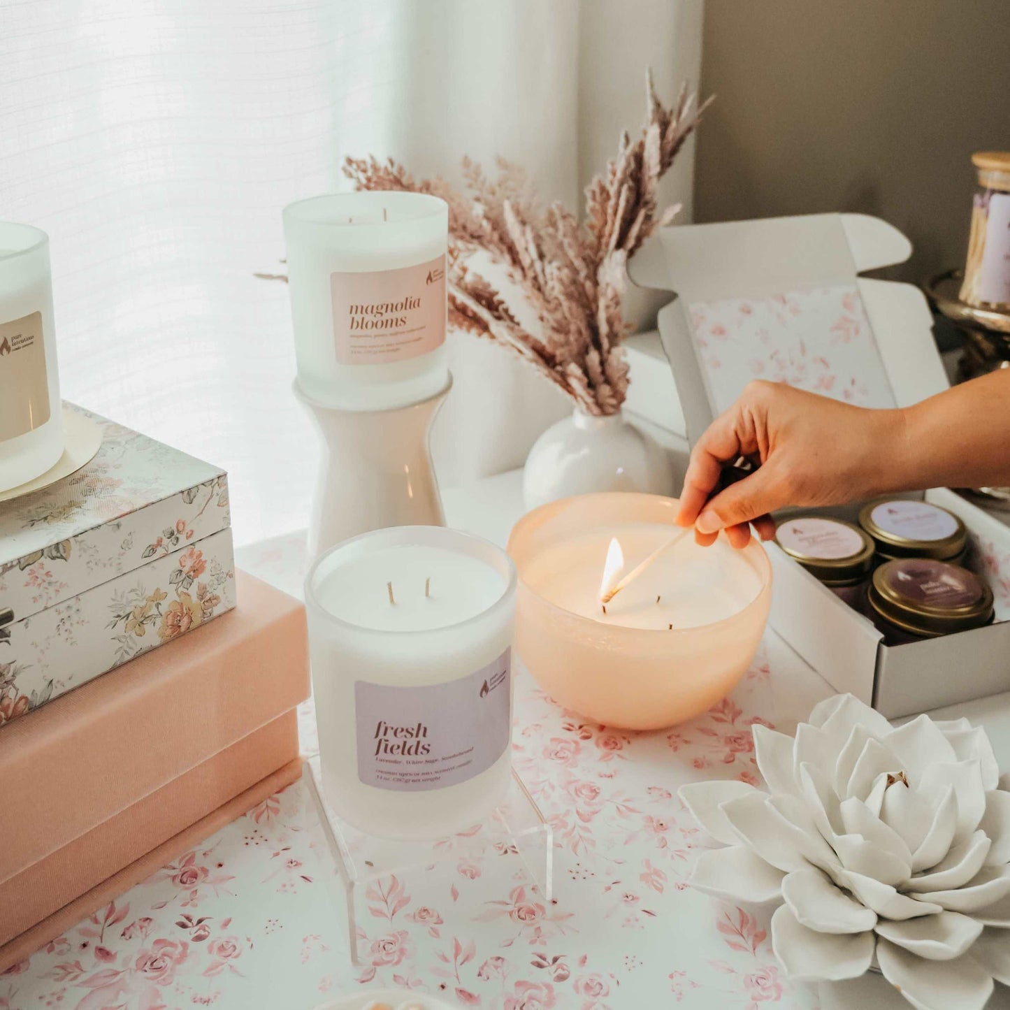 Candles on a table with a hand lighting one, surrounded by decorative items.