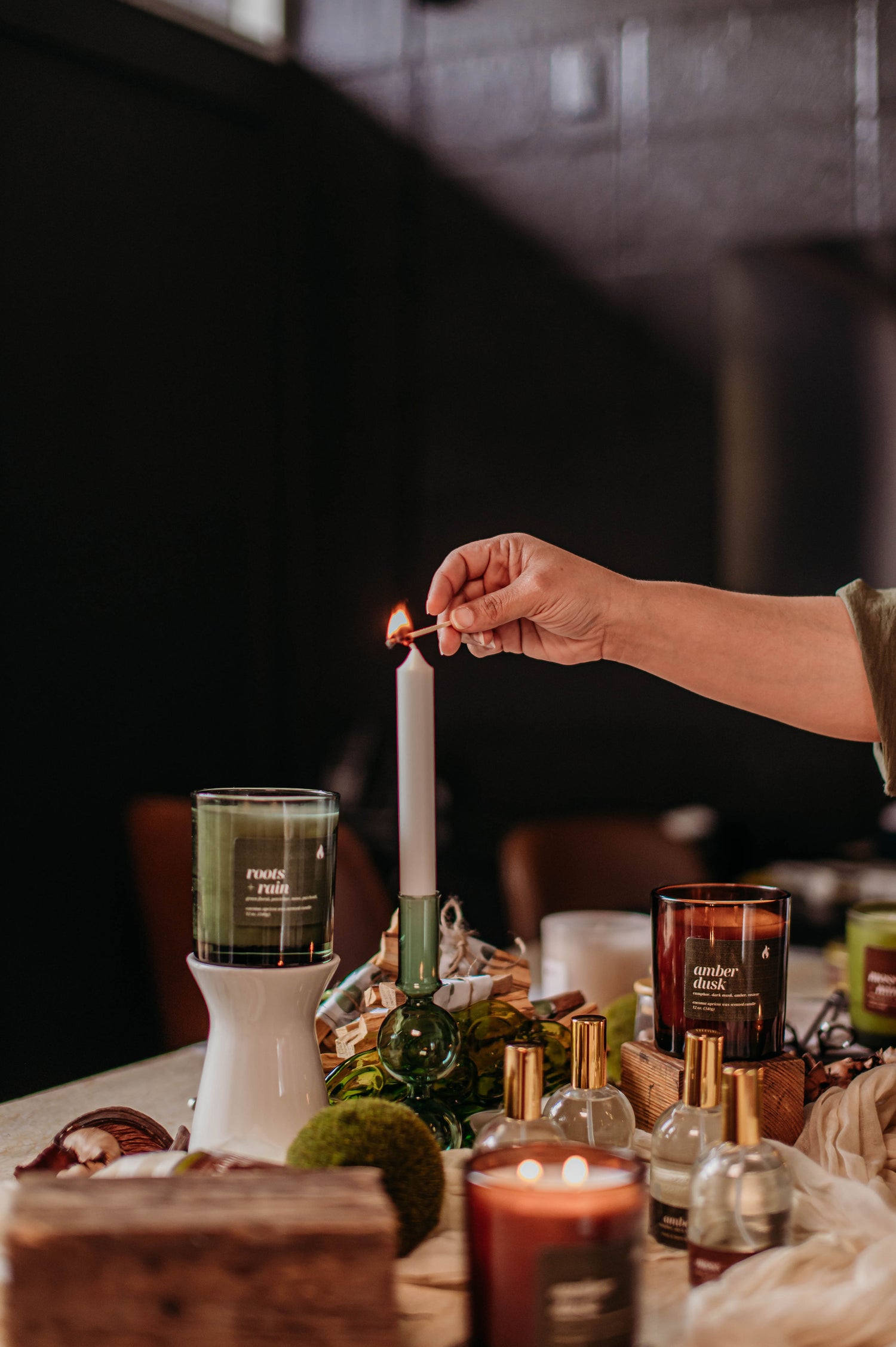Person lighting a candle with other candles and decorative items on a table.