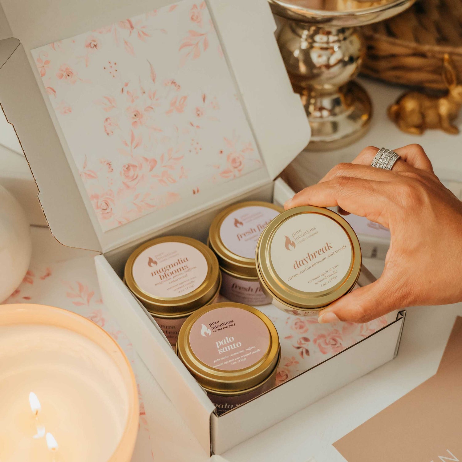 Candle packaging with floral design and a hand selecting a candle.
