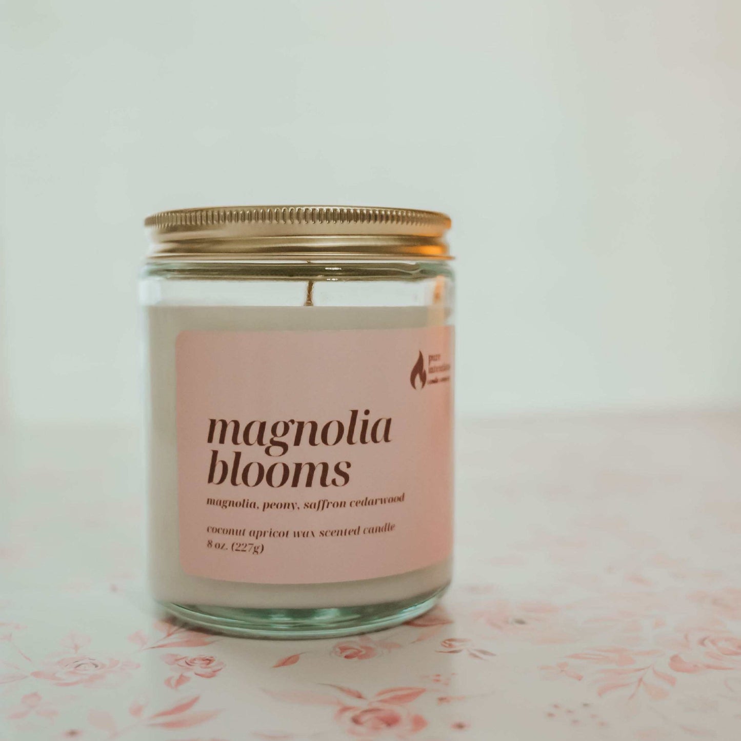 Candle jar labeled ' magnolia blooms' on a floral surface