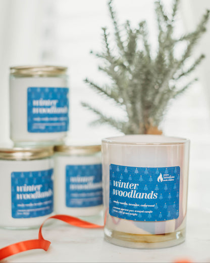 Candles labeled 'winter woodlands' with a plant in the background