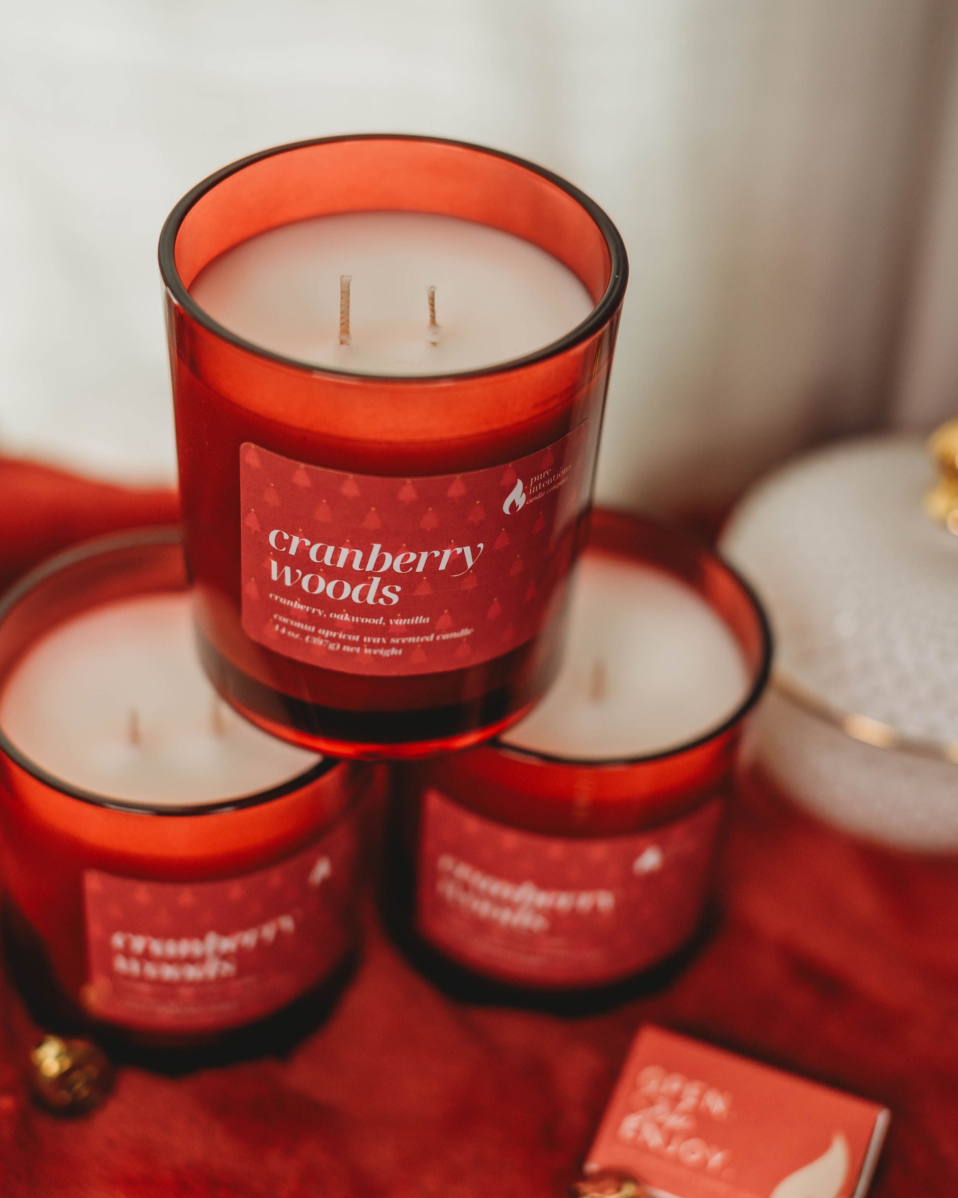 Red cranberry woods candles on a red surface with a blurred background