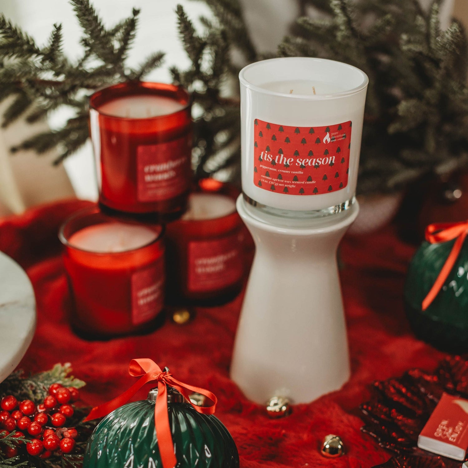 Decorative candles with festive design on a red surface with greenery