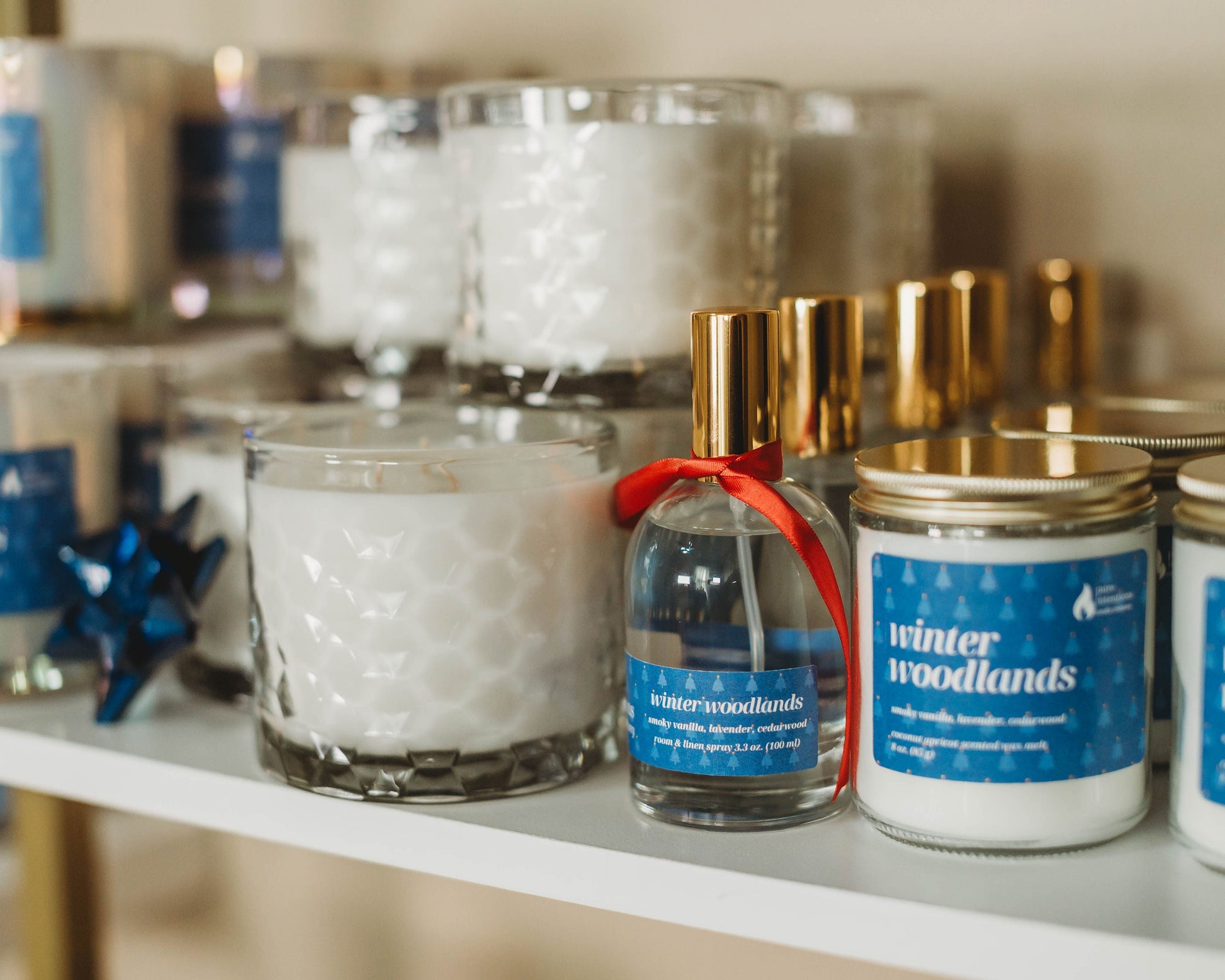 Candles and a small bottle with 'winter woodlands' label on a shelf.