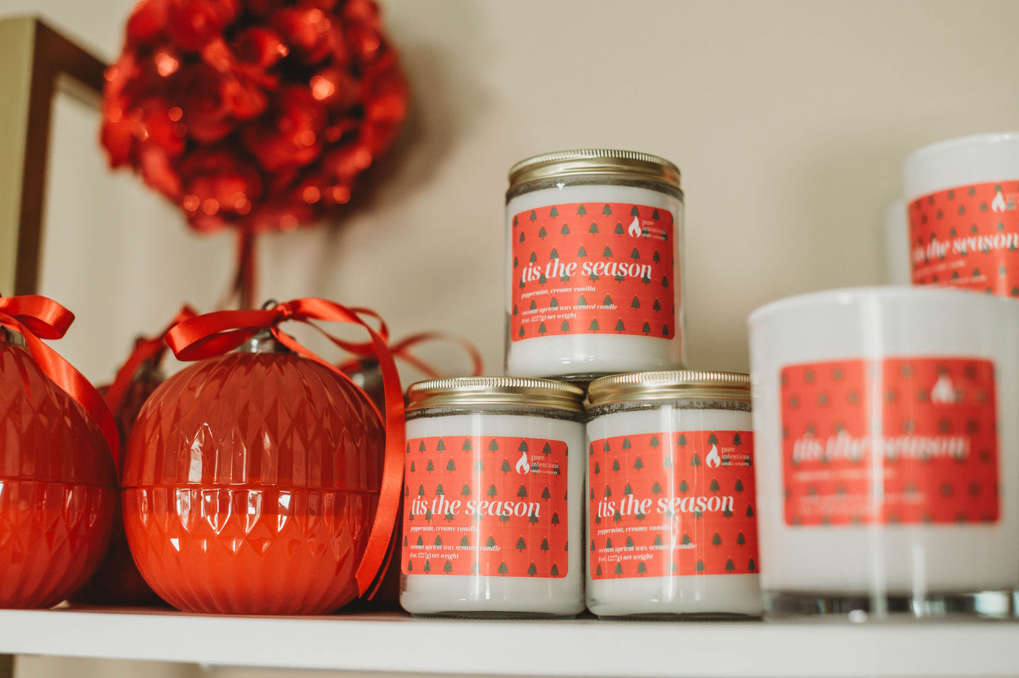Candles with 'this is the season' labels on a shelf with red decorative items.