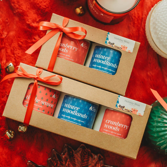 Box of holiday-themed candles with decorative green and red ornaments on a red surface.