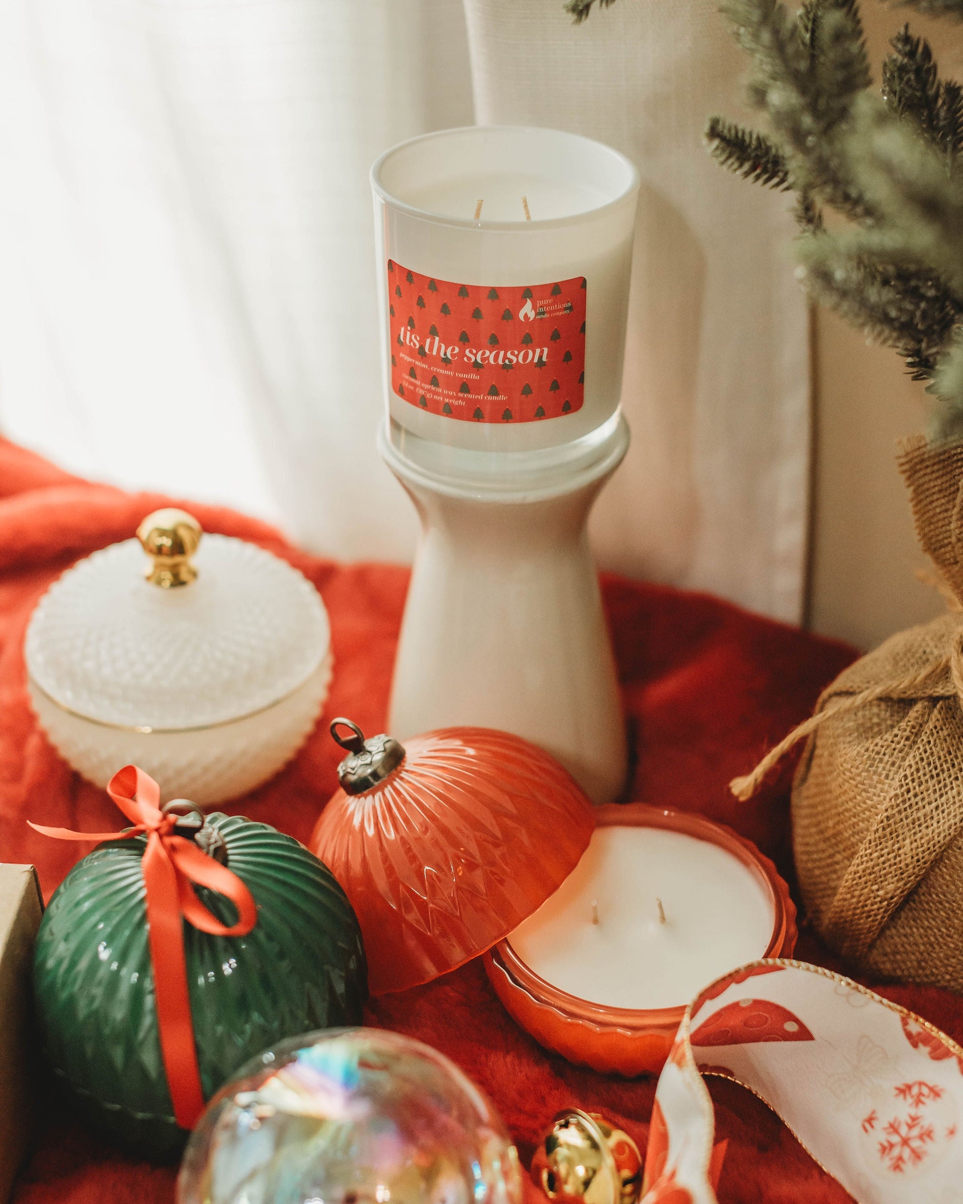 Decorative candles and ornaments on a red surface with a Christmas tree in the background