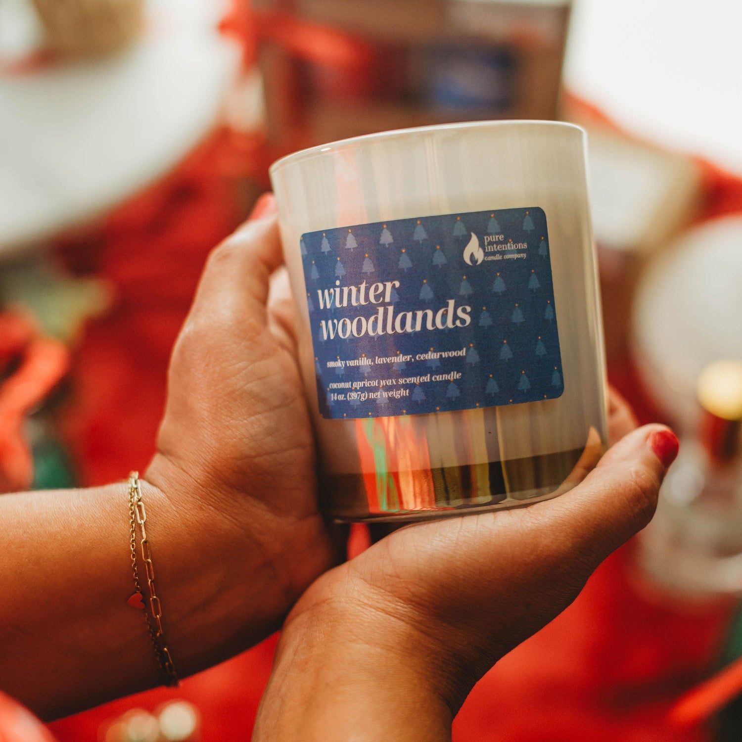 Person holding a candle labeled 'winter woodlands' with a festive background