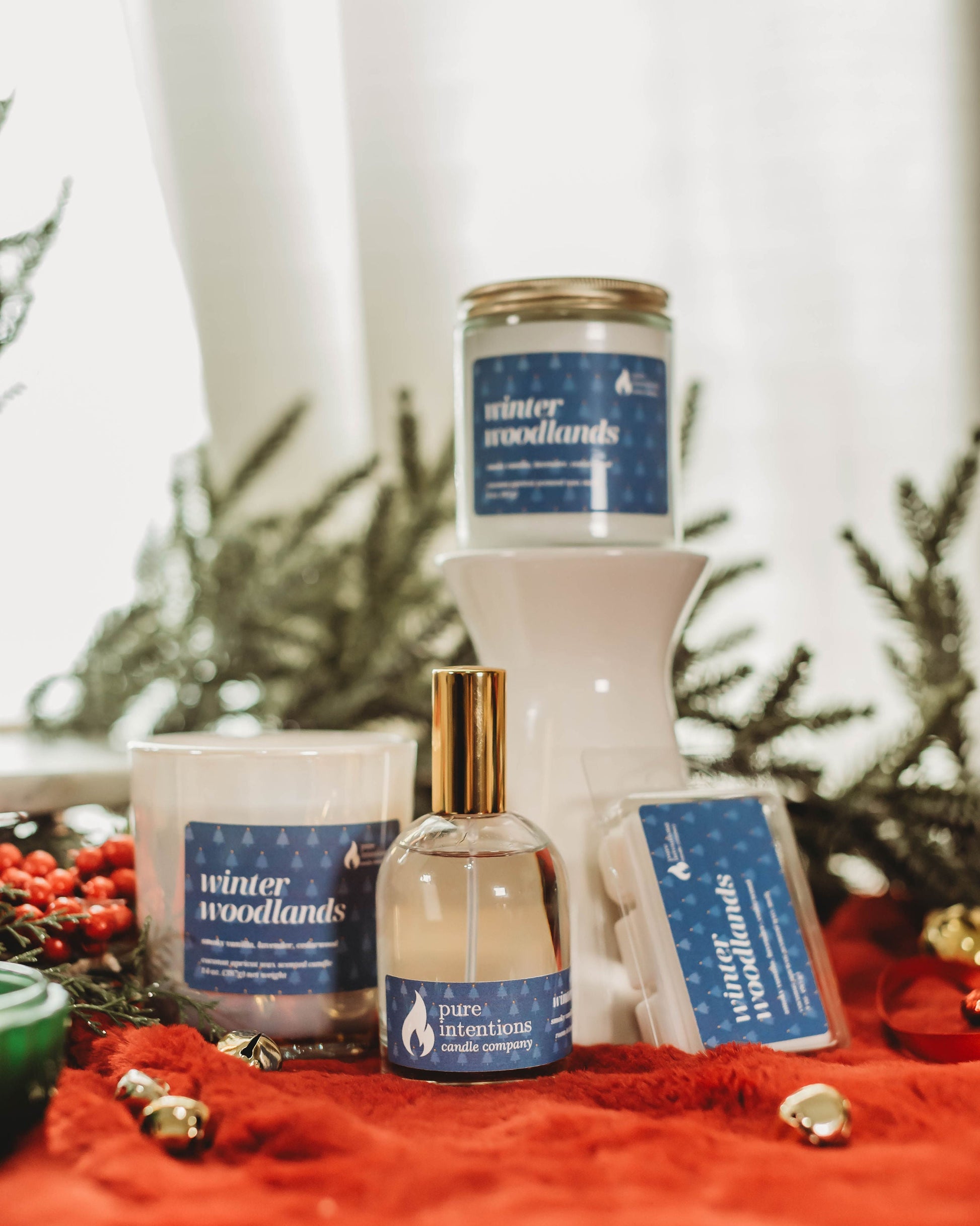 Collection of 'winter woodlands' themed candles and diffusers on a red surface with greenery in the background.