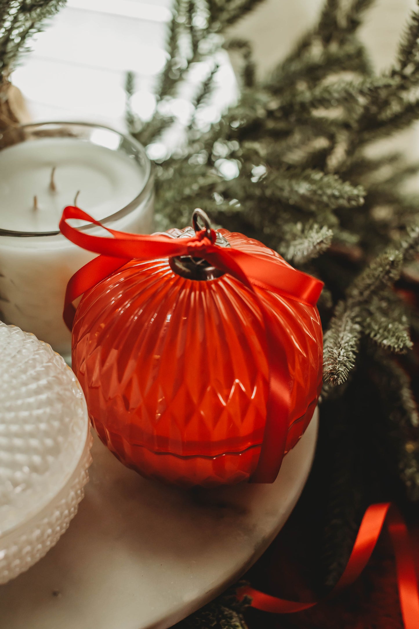 Red ornament on a white candle with a blurred Christmas tree in the background