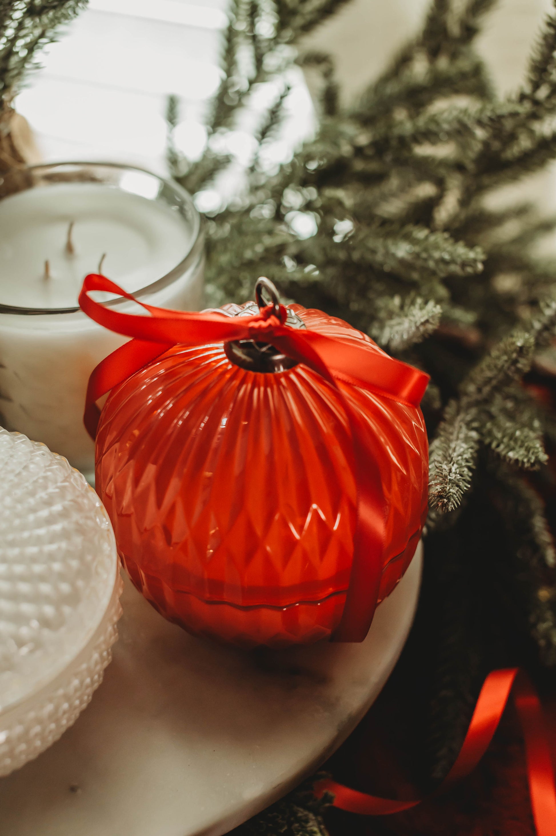 Red ornament on a white candle with a blurred Christmas tree in the background