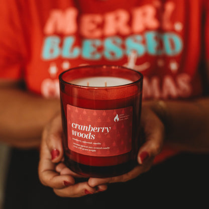 Person holding a 'Cranberry Woods' candle with a red shirt in the background