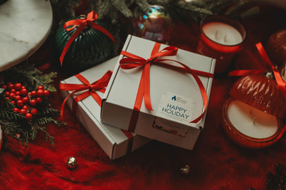 Gift boxes with red ribbons and 'Happy Holiday' card on a festive background with candles and decorations.