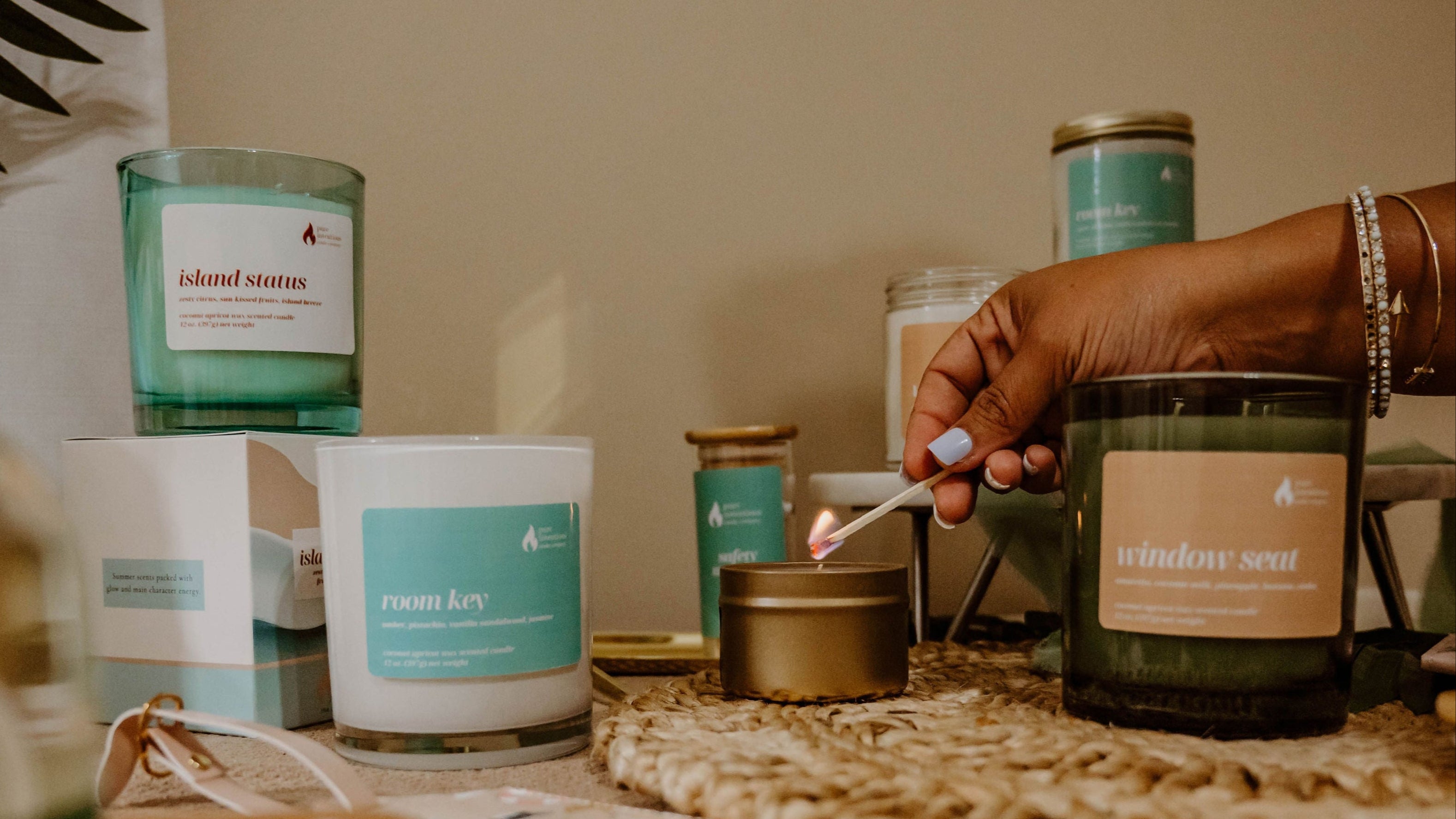 Candles on a table with a hand holding a lit candle, surrounded by various candles and decor items.
