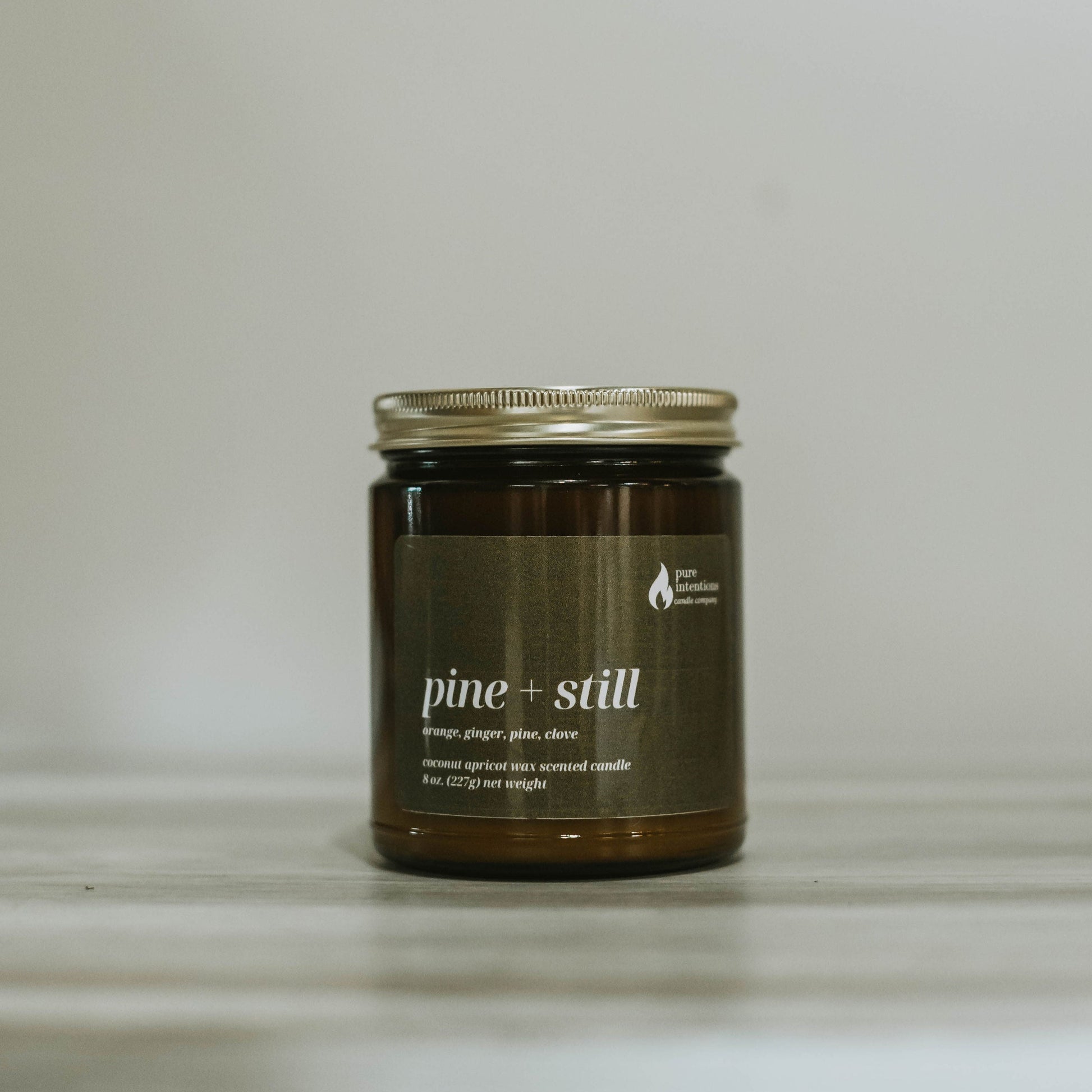Candle jar labeled 'pine + still' on a neutral background